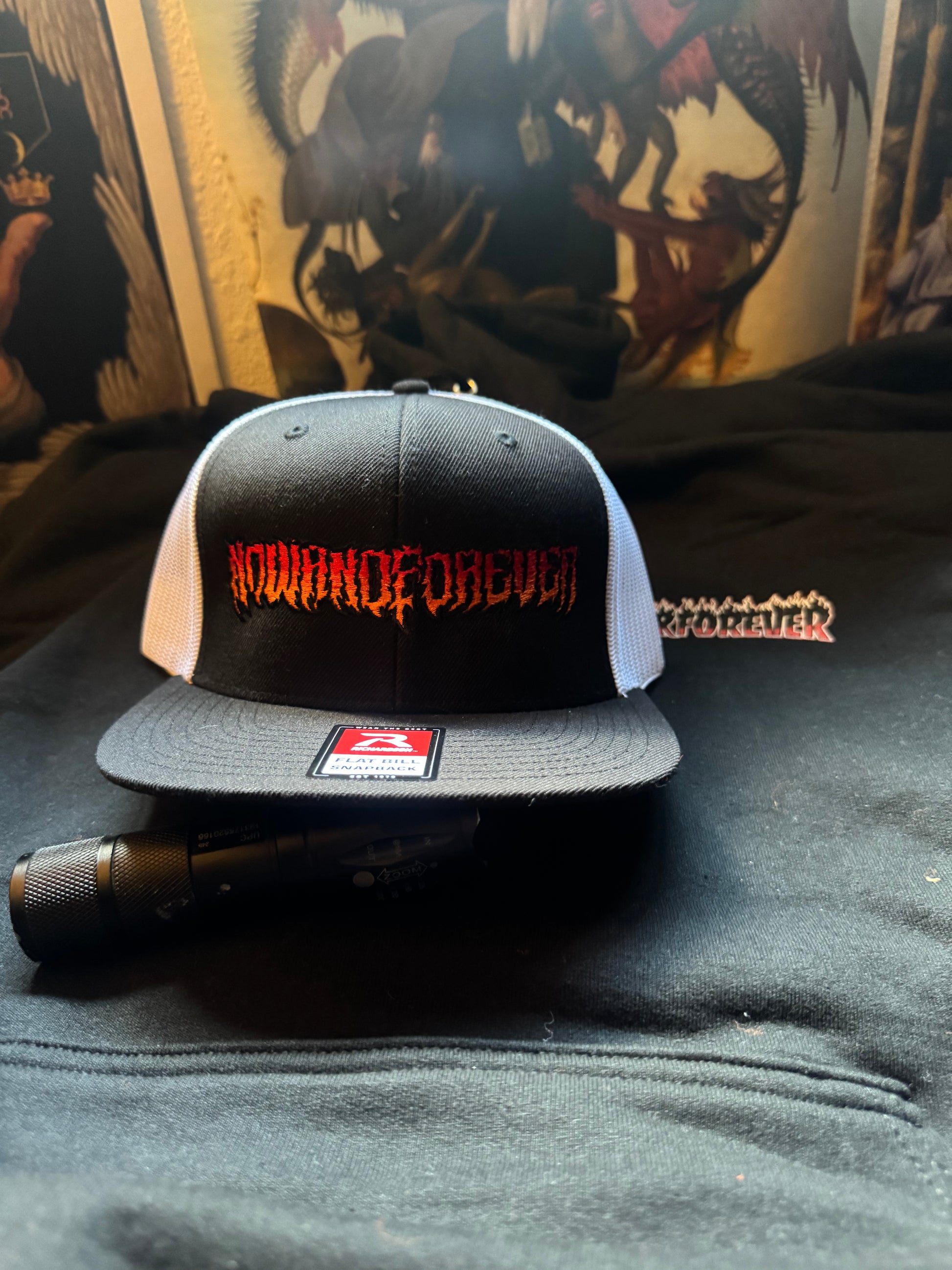 Now & Forever Industries graffiti wordmark trucker cap — black wool-blend front panel with the NOWANDFOREVER graffiti wordmark embroidered across it, flat bill, high crown, snapback closure