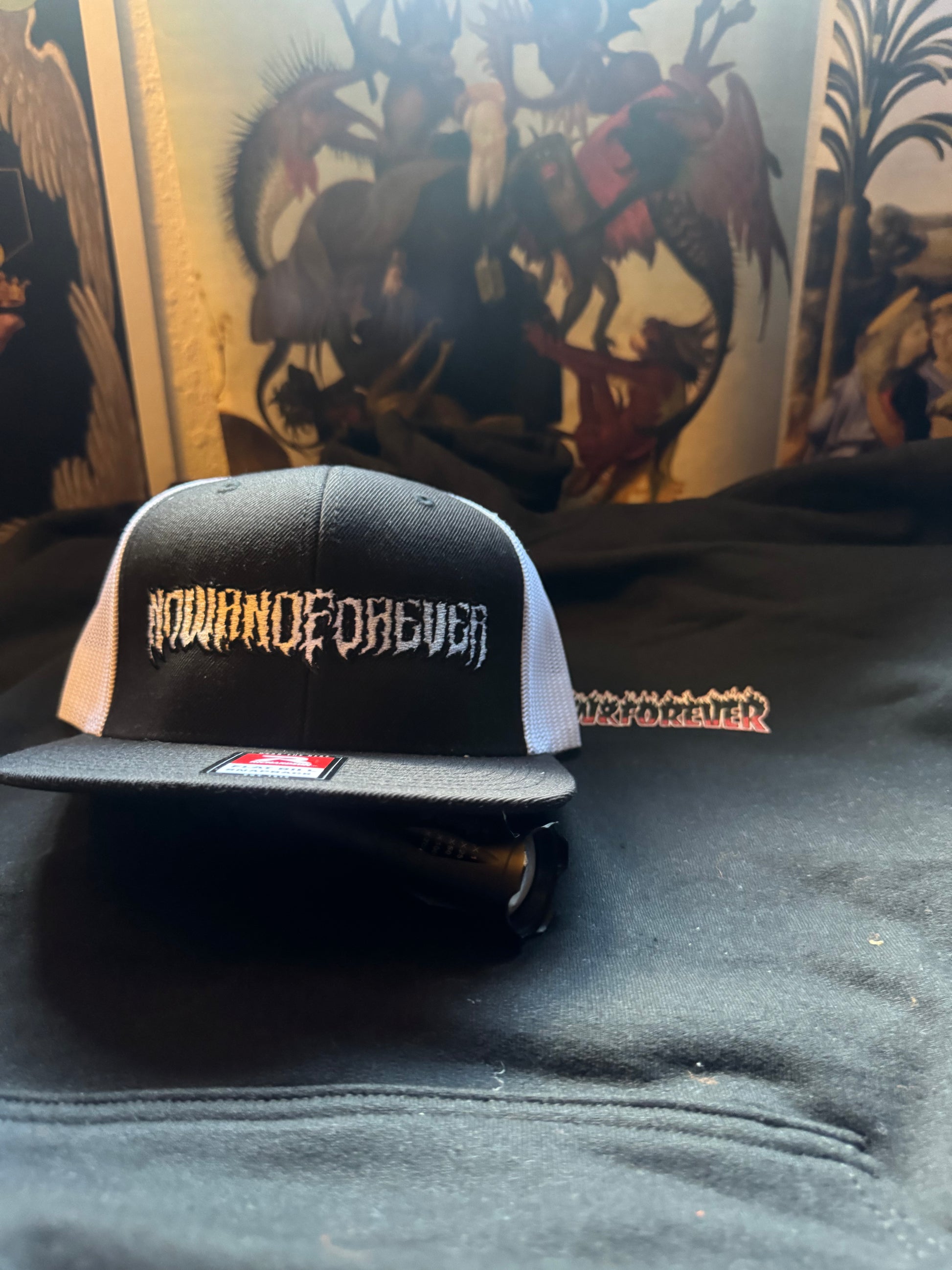 Close detail of the embroidered graffiti-style NOWANDFOREVER wordmark on the cap's black front panel